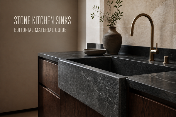 Dark honed natural-stone apron-front kitchen sink in warm wood cabinetry beneath a bronze-finish faucet, labeled Editorial Material Guide.