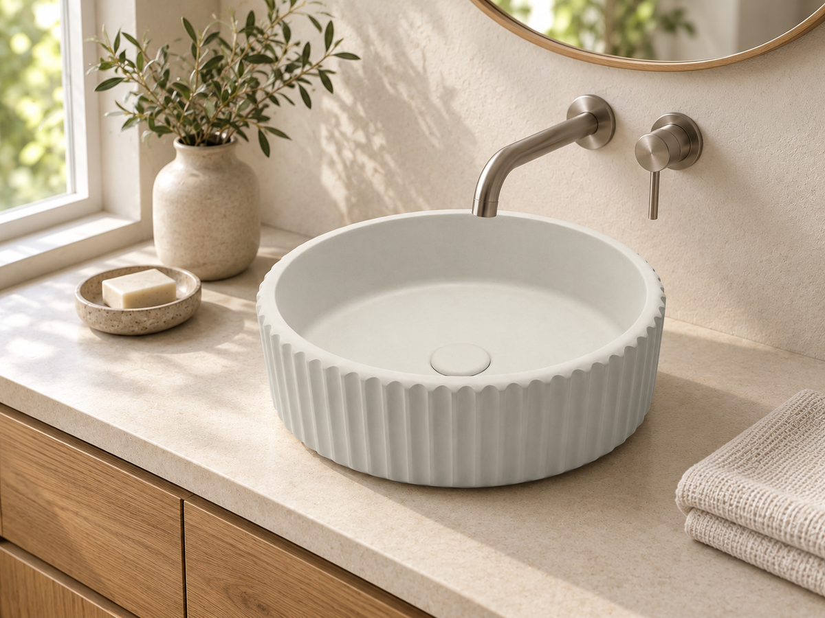 Off-white ribbed concrete vessel sink installed on an oak bathroom vanity with a wall-mounted faucet.