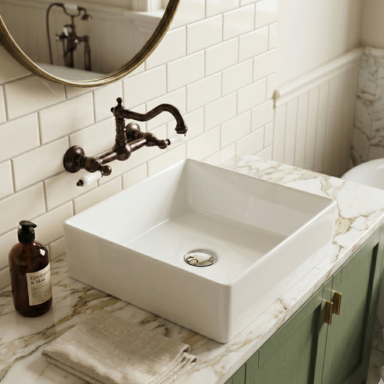 White square ceramic vessel sink on a marble countertop with wall-mounted faucet and green vanity in a subway-tile bathroom